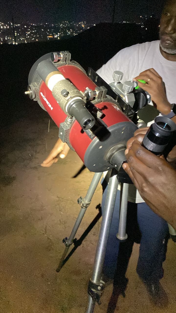 Adjusting a telescope under the night sky with city lights beyond